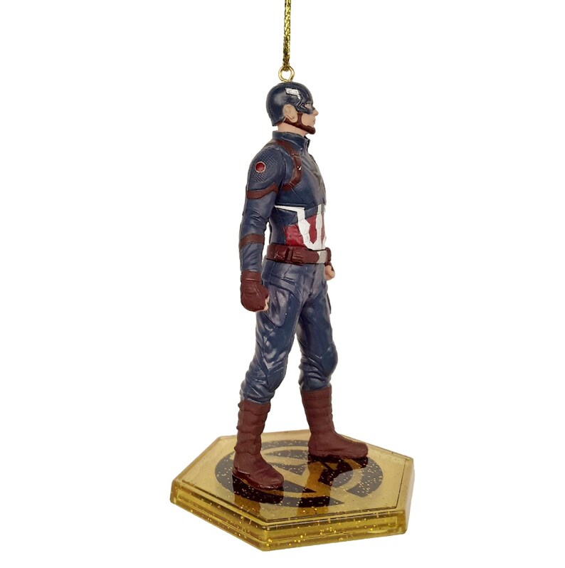 May include: A Captain America figurine ornament. The figurine is wearing a blue and red uniform with a brown belt and boots. The ornament hangs from a gold string and is standing on a gold base.