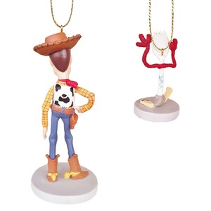 May include: A set of two Christmas ornaments featuring Woody and Forky from the Toy Story movie franchise. Woody is wearing his signature cowboy hat and vest, while Forky is a spork with googly eyes and red pipe cleaner arms.