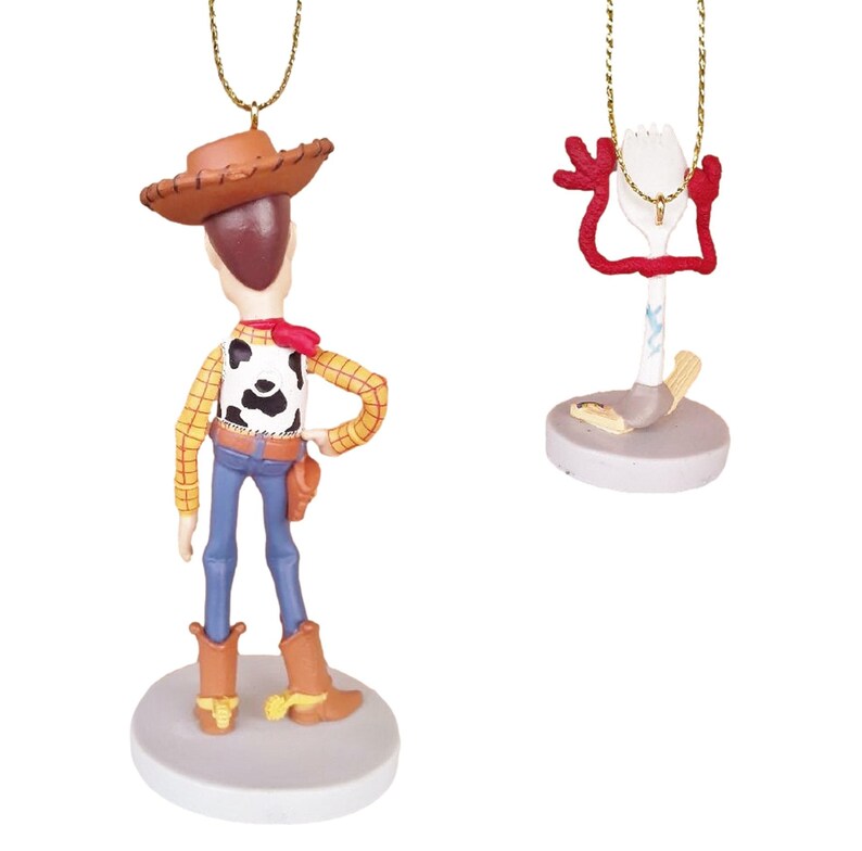 May include: A set of two Christmas ornaments featuring Woody and Forky from the Toy Story movie franchise. Woody is wearing his signature cowboy hat and vest, while Forky is a spork with googly eyes and red pipe cleaner arms.