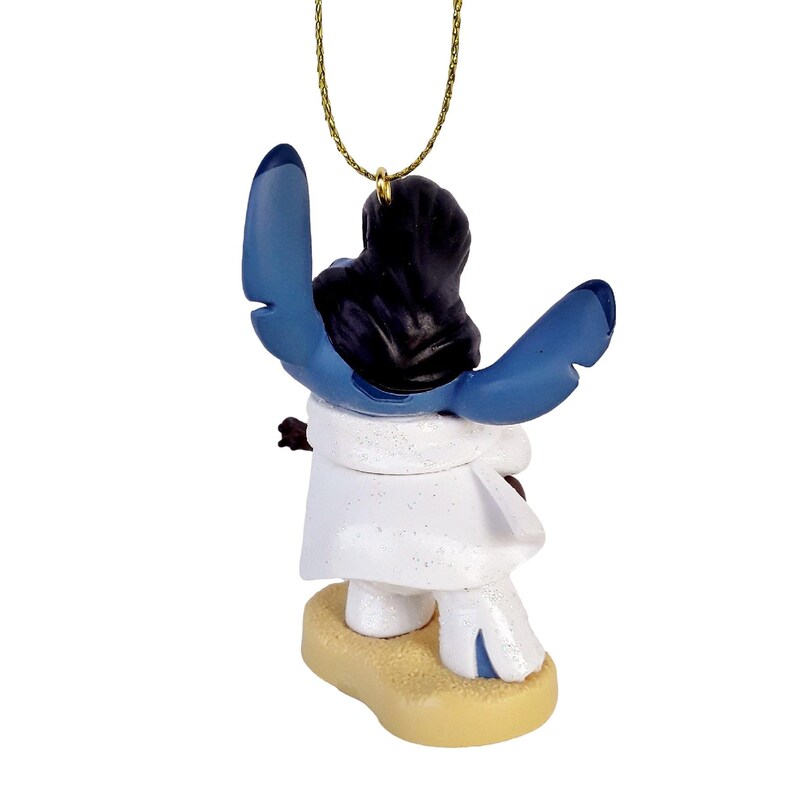 Puede incluir: Una figura azul y negra de un personaje con orejas grandes y un atuendo blanco. La figura est&aacute; unida a una cadena dorada. El personaje est&aacute; de pie sobre una base de color canela.
