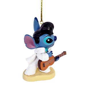 Puede incluir: Adorno de personaje azul con un peinado pompadour negro, que lleva un traje blanco y sostiene una guitarra marr&oacute;n. El adorno est&aacute; sobre una base beige y tiene una cuerda dorada para colgar.