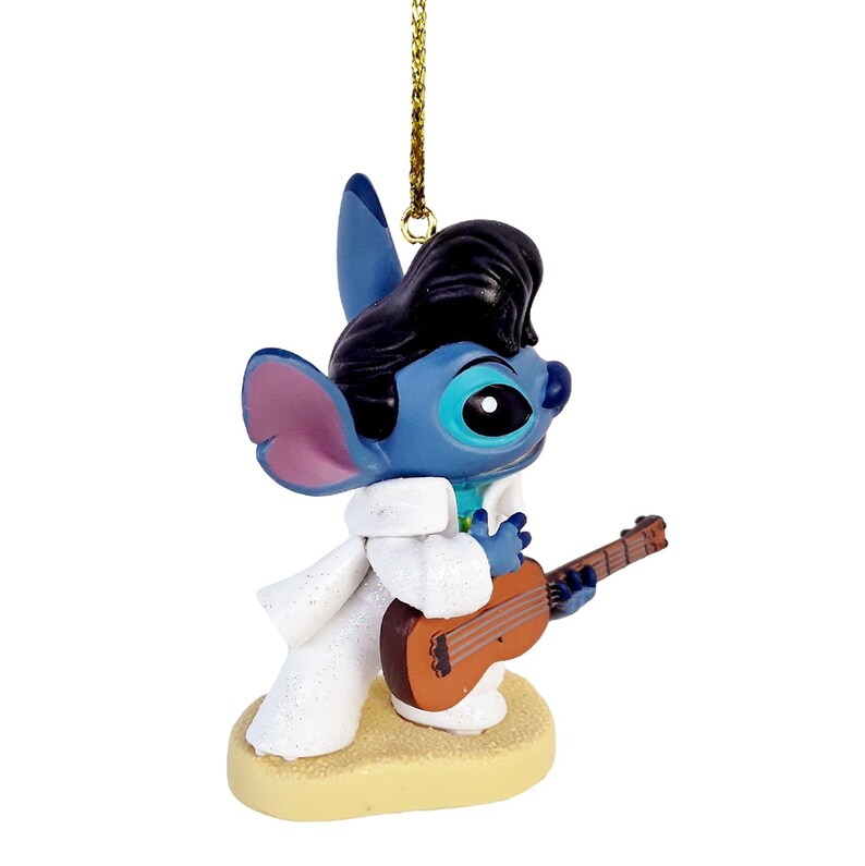 Puede incluir: Adorno de personaje azul con un peinado pompadour negro, que lleva un traje blanco y sostiene una guitarra marr&oacute;n. El adorno est&aacute; sobre una base beige y tiene una cuerda dorada para colgar.