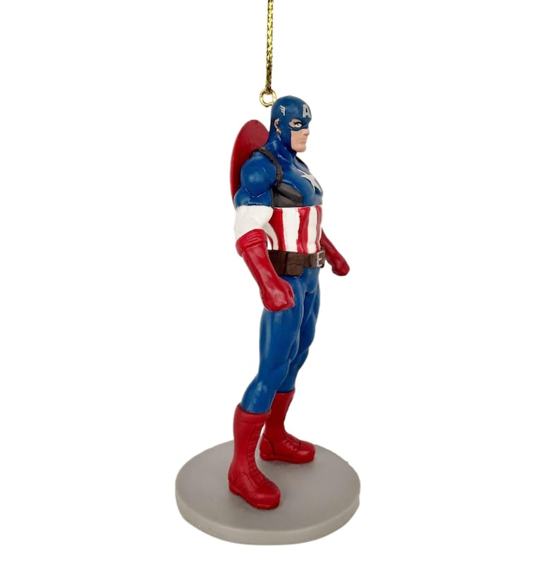May include: A Captain America figurine in a classic pose, featuring a blue and red costume with a white star on the chest. The figurine has a red shield on its back and is mounted on a gray circular base. A gold string is attached for hanging.