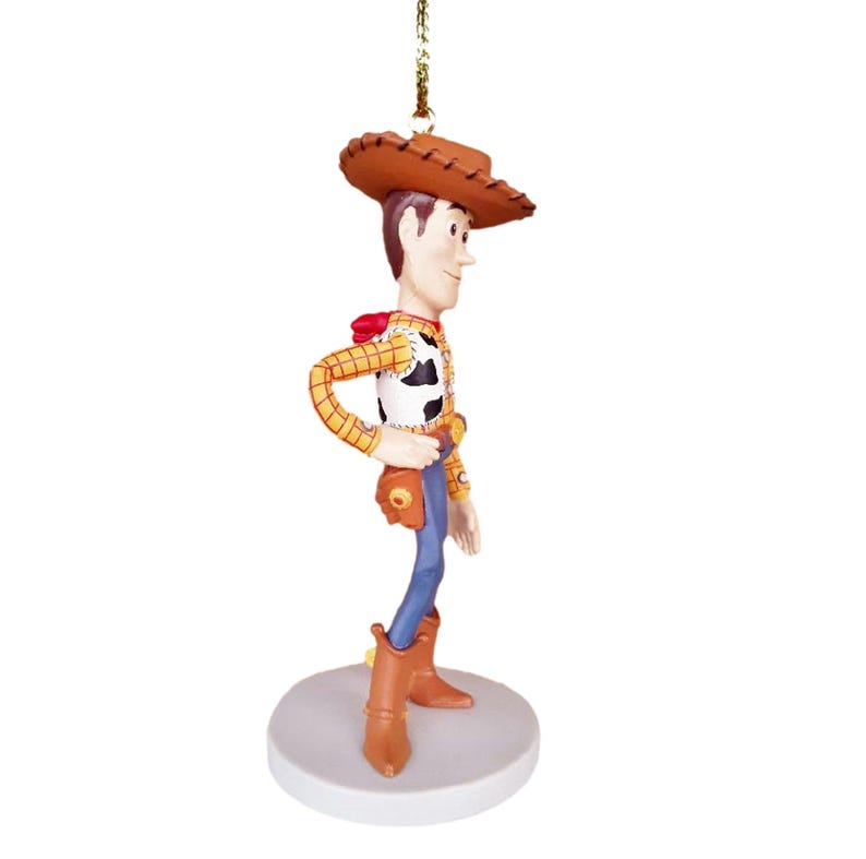 Puede incluir: Un adorno de figura de vaquero marr&oacute;n y blanco con un sombrero marr&oacute;n, pantalones vaqueros azules y una camisa a cuadros amarillo y rojo. La figura est&aacute; de pie sobre una base blanca.