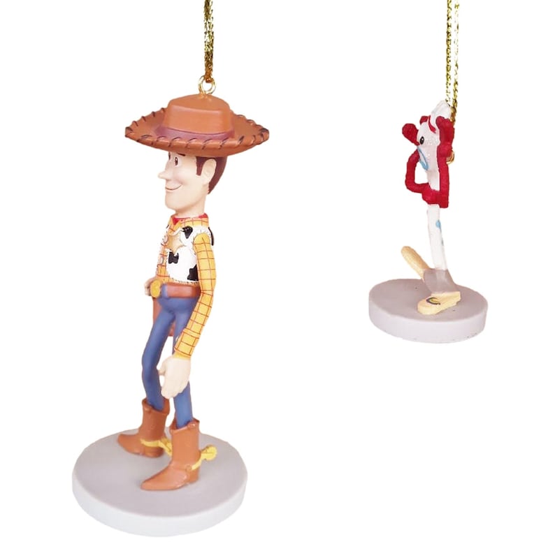 May include: A set of two Christmas ornaments featuring Woody and Buzz Lightyear from the Toy Story franchise. Woody is wearing his signature cowboy hat and vest, while Buzz is in his space ranger suit. Both ornaments are made of plastic and have a gold string for hanging.