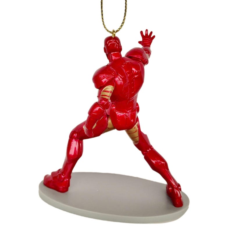 May include: A red Iron Man figurine in a dynamic pose, with one arm raised. The figure has gold accents and is attached to a gold-colored chain. It stands on a gray oval base, perfect for display.