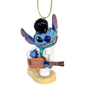 Puede incluir: Una figura azul de Stitch vestido como Elvis Presley, con un traje blanco y sosteniendo un ukelele marr&oacute;n. La figura tiene cabello negro y est&aacute; sonriendo. Est&aacute; sujeta a una cuerda dorada para colgar.