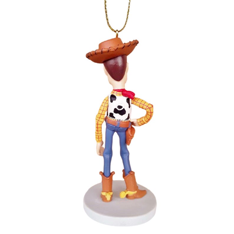 Puede incluir: Una figura de vaquero marr&oacute;n y amarillo con un pa&ntilde;uelo rojo y un sombrero marr&oacute;n. La figura est&aacute; de pie sobre una base blanca y sostiene una pistola en su mano derecha.