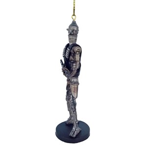 Pu&ograve; includere: Un ornamento di robot argentato e nero con una corda dorata appesa in cima. Il robot tiene una pistola nella mano destra e ha un design dettagliato.