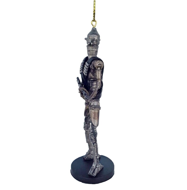 Pu&ograve; includere: Un ornamento di robot argentato e nero con una corda dorata appesa in cima. Il robot tiene una pistola nella mano destra e ha un design dettagliato.