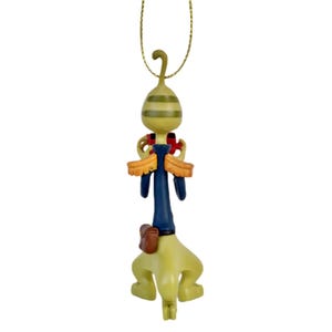 May include: A whimsical Christmas ornament featuring a stylized figure with a green and yellow striped head, blue torso, and yellow legs. The ornament has a gold hanging string and is decorated with red and brown accents.