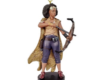 May include: A brown and gold figurine of a woman with dark brown hair holding a bow and arrow. She is wearing a brown vest, purple pants, and a brown cape. The figurine is standing on a black base.