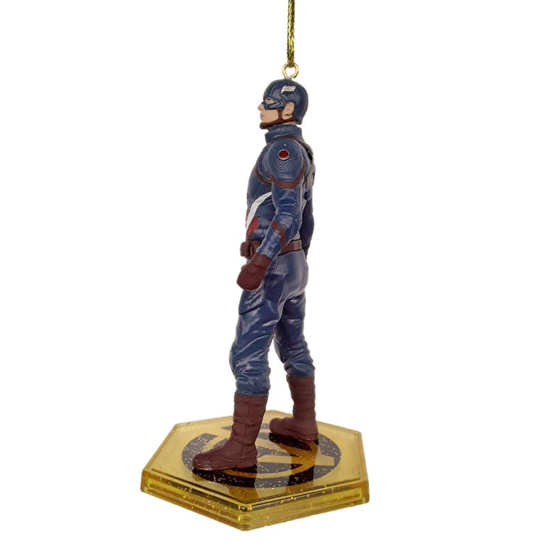 May include: A Captain America figurine in a standing pose, wearing a blue and red costume with a helmet. The figurine is attached to a gold-colored hexagonal base with the Avengers logo. A gold string is attached to the top for hanging.