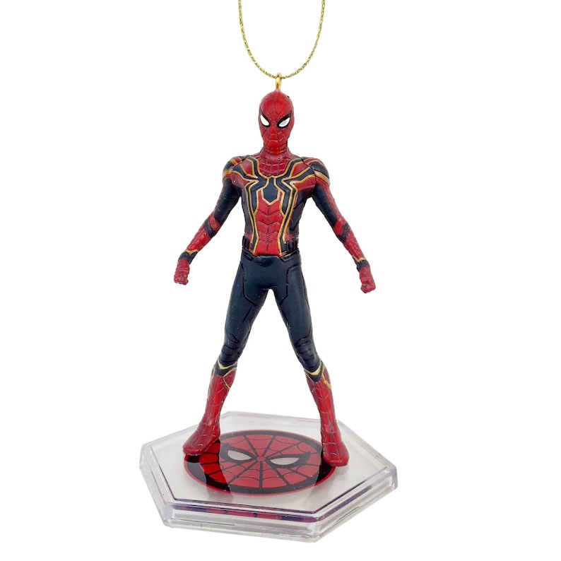 May include: A Spider-Man figure in a standing pose, featuring a red and gold suit with black accents. The figure is attached to a gold-colored string and sits on a clear, hexagonal base with a red spider-web design.