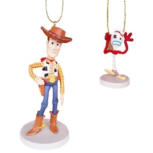 May include: Two Christmas ornaments featuring characters from the Toy Story franchise. The first ornament is a 3D depiction of Woody, the cowboy doll, wearing his signature brown hat, yellow vest, and blue jeans. The second ornament is a 3D depiction of the toy, Forky, with his red, white, and blue construction paper body and googly eyes.