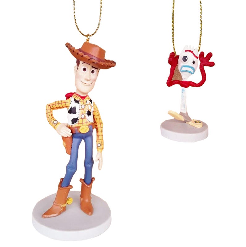 May include: Two Christmas ornaments featuring characters from the Toy Story franchise. The first ornament is a 3D depiction of Woody, the cowboy doll, wearing his signature brown hat, yellow vest, and blue jeans. The second ornament is a 3D depiction of the toy, Forky, with his red, white, and blue construction paper body and googly eyes.