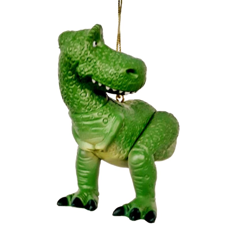 Puede incluir: Adorno de pl&aacute;stico verde de un dinosaurio de la franquicia de pel&iacute;culas Toy Story. El dinosaurio est&aacute; de pie sobre sus cuatro patas con la cabeza girada hacia un lado. El adorno tiene una cuerda dorada para colgar.