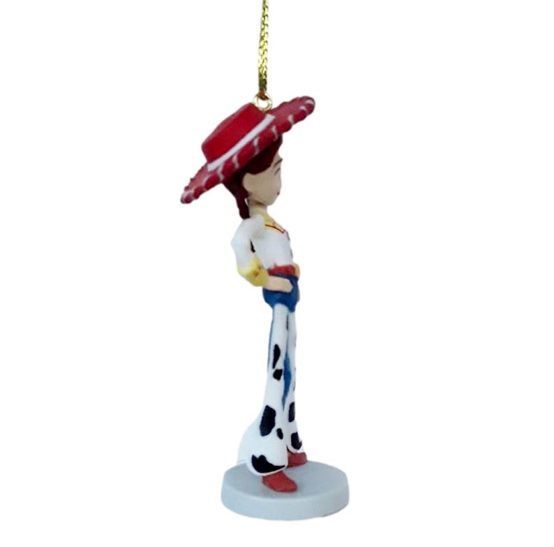 May include: A small, decorative figurine of a character from the animated film Toy Story. The figurine is wearing a red hat with white trim, a white shirt with yellow accents, blue pants, and black and white spotted chaps. It is attached to a gold string.