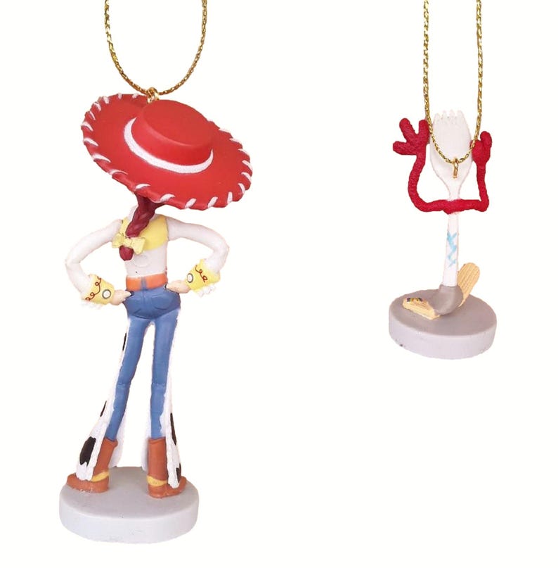 May include: Two Toy Story character ornaments, one of Jessie the cowgirl with a red hat and blue jeans, and the other of Forky with a red, white, and blue body.