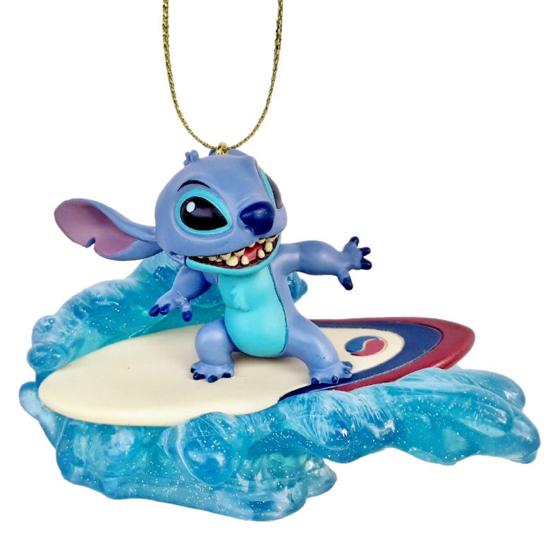 May include: A blue Stitch figurine surfing on a surfboard, with a gold-colored string for hanging. The figurine is on a blue wave base. The surfboard has red, white, and blue accents.