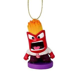 May include: A red, cartoon-style ornament of the character Anger from the movie Inside Out. The ornament has a yellow flame-like head, a white shirt, and purple pants. It is attached to a gold-colored string.