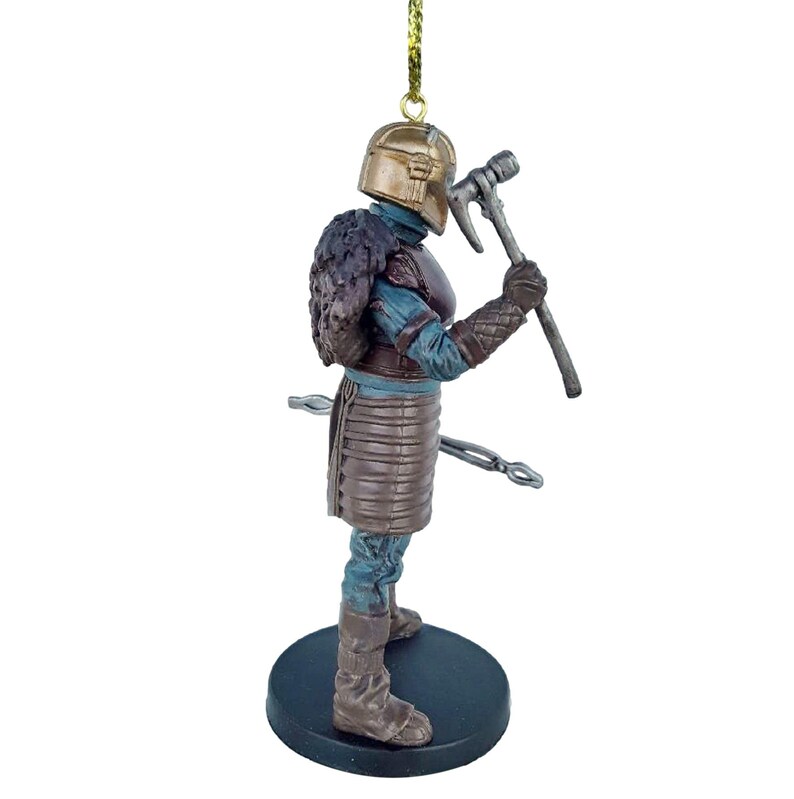May include: A brown and gold ornament of a warrior figure with a helmet, fur, and a weapon. The figure is standing on a black base.