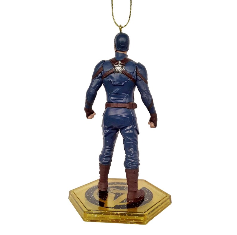 May include: A Captain America figurine, viewed from the back, stands on a gold-colored hexagonal base. The figurine is dressed in a blue suit with brown accents and boots. A gold string is attached to the top of the figurine for hanging.