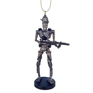 Pu&ograve; includere: Un ornamento natalizio a tema Star Wars in argento e nero con un droide che tiene una pistola. L'ornamento &egrave; appeso a un filo dorato.