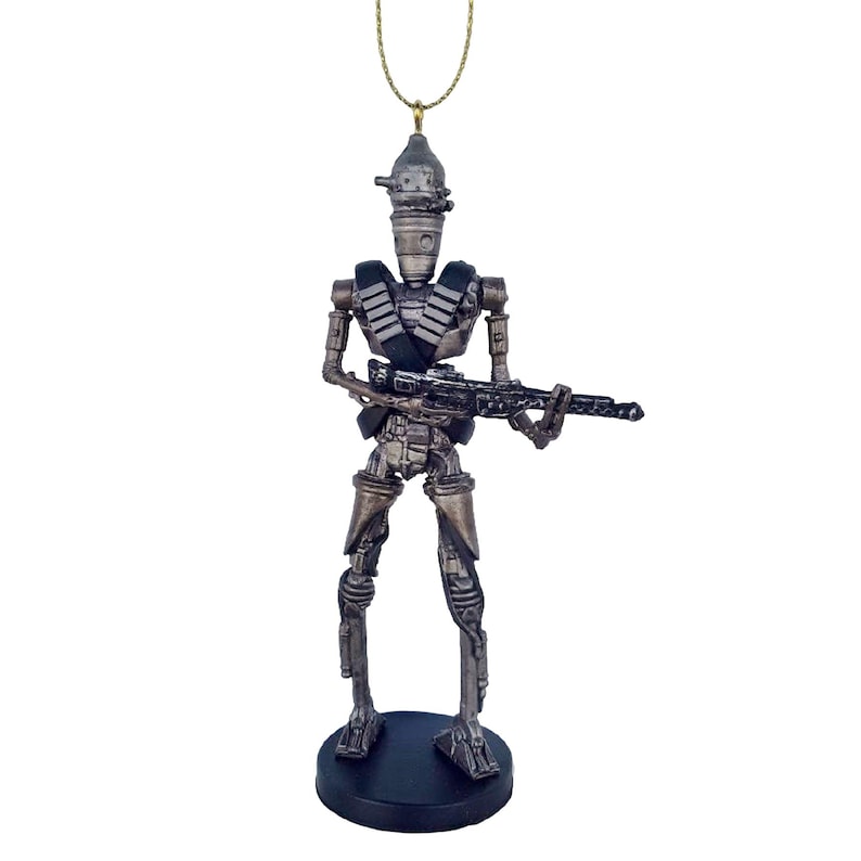 Pu&ograve; includere: Un ornamento natalizio a tema Star Wars in argento e nero con un droide che tiene una pistola. L'ornamento &egrave; appeso a un filo dorato.