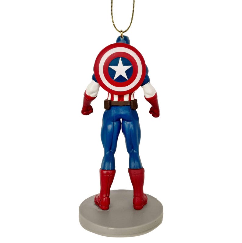 May include: A Captain America figurine ornament, viewed from the back. The figure is in a classic superhero pose, wearing a blue suit, red boots, and a shield with a white star on a red and white background. The ornament hangs from a gold string.