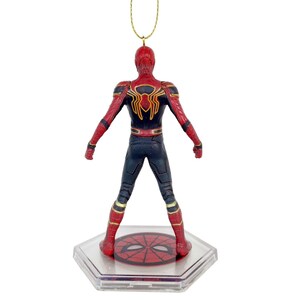 May include: A Spider-Man figure, viewed from the back, in a dynamic pose. The figure is predominantly red and black, with gold accents. It stands on a clear, hexagonal base with a Spider-Man emblem. A gold string is attached for hanging.