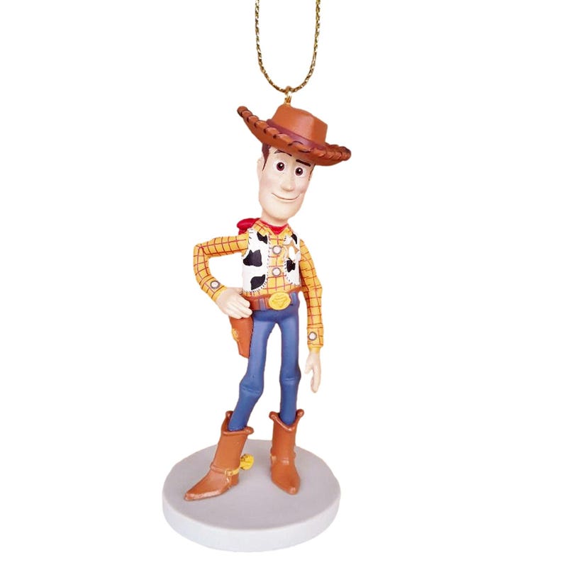 Puede incluir: Una figura de vaquero marr&oacute;n y amarillo que lleva un sombrero marr&oacute;n y pantalones vaqueros azules. La figura sostiene una pistola en su mano derecha y tiene una estrella de sheriff en su pecho. La figura est&aacute; de pie sobre una base blanca.