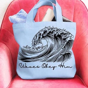 May include: A light blue canvas tote bag featuring a black ink-style illustration of a large crashing ocean wave. The text "Even the WIND and Waves Obey Him" is printed in black script and block lettering across the center of the bag.