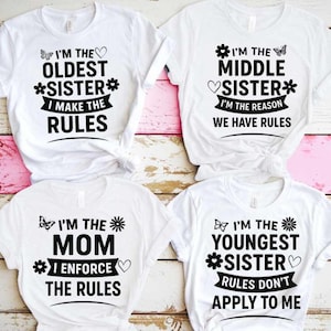 May include: Four white t-shirts with black text and graphics. The shirts read "I'm the Oldest Sister I Make the Rules", "I'm the Middle Sister I'm the Reason We Have Rules", "I'm the Mom I Enforce the Rules", and "I'm the Youngest Sister Rules Don't Apply to Me".