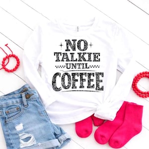 May include: A white long-sleeved top with the black text "NO TALKIE UNTIL COFFEE". The image includes denim shorts, bright pink socks, and red beaded bracelets. This is a casual wear item.