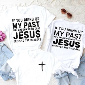 Puede incluir: Camisetas blancas con texto negro: "IF YOU BRING UP MY PAST YOU SHOULD KNOW THAT JESUS DROPPED THE CHARGES." Una camiseta tiene una cruz. Gafas de sol y vaqueros también son visibles en la imagen.