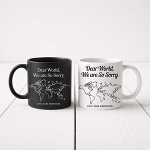 Pode incluir: Duas canecas de cerâmica, uma preta e outra branca, com um contorno do mapa-múndi e o texto "Dear World, We are So Sorry" em preto. A caneca preta tem uma alça preta, e a caneca branca tem uma alça branca. O texto "LOVE, SANE AMERICANS" está impresso abaixo.