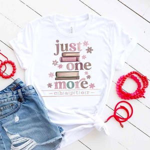 May include: White t-shirt with the text "just one more chapter" in a stacked design with book illustrations and floral accents. The shirt is paired with denim shorts and red beaded bracelets.