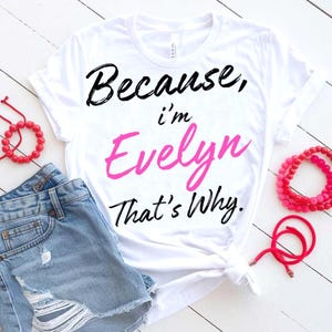 May include: White t-shirt with the text "Because, I'm Evelyn That's Why" in black and pink. The shirt is paired with denim shorts and red bracelets. The shirt is knotted at the waist.