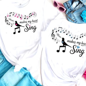 May include: White t-shirts with a musical theme. Each shirt features a black bird perched on musical notes, with the text "Music makes my heart Sing". One shirt has pink accents, the other blue.
