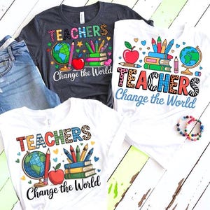 May include: Three white and gray t-shirts with the word "TEACHERS" in colorful letters and the phrase "Change the World". Each shirt features a globe, apple, pencils, and books. A pair of blue jeans and a beaded bracelet are also visible.