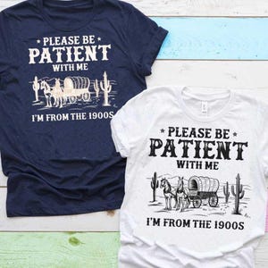 以下が含まれることがあります： 紺色と白の2枚のTシャツ。テキストは「PLEASE BE PATIENT WITH ME I'M FROM THE 1900S」です。各シャツには、幌馬車、馬、サボテンのグラフィックが描かれています。