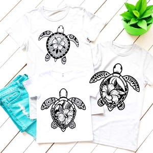 May include: White t-shirts with a black turtle design. The turtle design features a floral pattern within the shell. The shirts are displayed with a pair of blue denim shorts and a small green plant in a green pot.