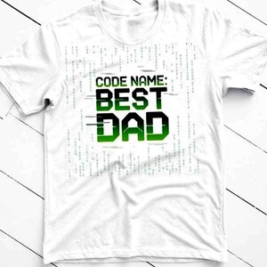 May include: White t-shirt with the text "CODE NAME: BEST DAD" in a green and black gradient font. The design includes a digital rain pattern in the background, giving it a tech-inspired look. A perfect gift for Father's Day.