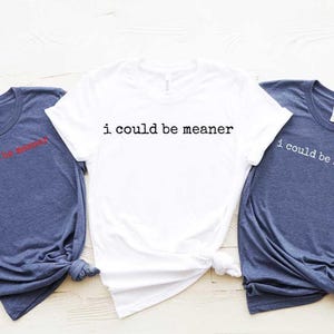 May include: Two t-shirts with the text "i could be meaner" printed on them. One t-shirt is white and the other is blue.