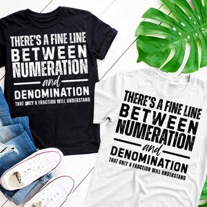 Op de afbeelding: Zwarte en witte t-shirts met de tekst "THERE'S A FINE LINE BETWEEN NUMERATION and DENOMINATION THAT ONLY A FRACTION WILL UNDERSTAND." De shirts worden gecombineerd met een blauwe jeans en witte sneakers.