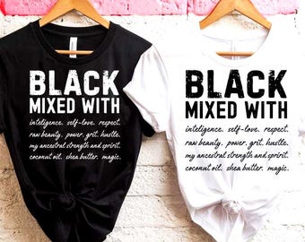 May include: Two t-shirts, one black and one white, hanging on wooden hangers. Each shirt features the text "BLACK MIXED WITH" in bold, white letters. Below the text are additional words in a smaller font.