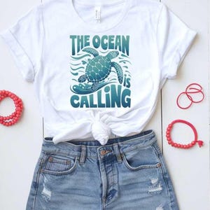 May include: White t-shirt with a blue and green sea turtle graphic and the text "The Ocean is Calling".