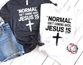 Può includere: Due magliette, una grigio scuro e una bianca, con la scritta "NORMAL isn't coming back, JESUS IS" e una croce. La maglietta grigio scuro è abbinata a pantaloncini di jeans. È visibile anche un braccialetto di perline.