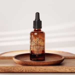 May include: A brown glass bottle with a black dropper top, containing a liquid. The bottle has a gold decorative label with the text "RUSTIC GOOD BEAUTY PRODUCTS GROW THRIVE GLOW". It sits on a wooden tray.